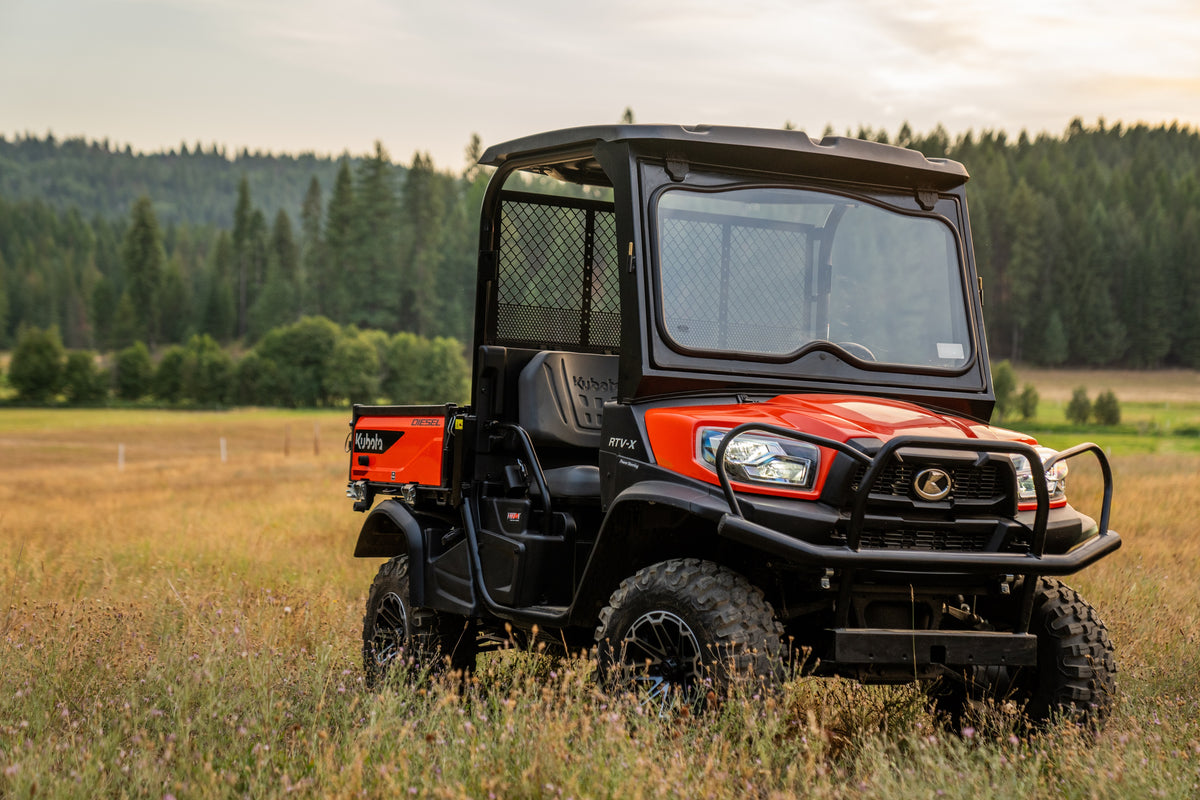 Kubota RTV-X utility vehicle in orange with a roof and windshield, in a meadow