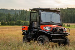 Kubota RTV-X utility vehicle in orange with a roof and windshield, in a meadow