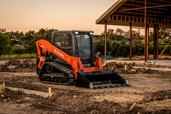 Kubota SVL series compact track loader with a toothed bucket on a building site at dusk, its work lights on