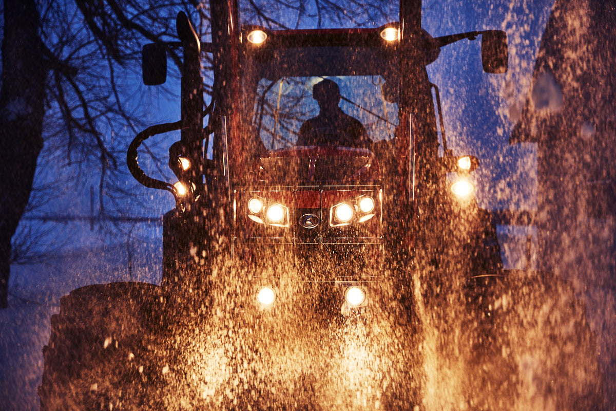 Kubota M7 tractor with bale spear working at night in the snow.