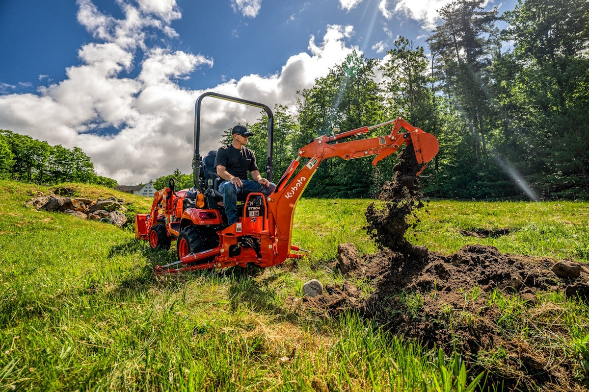 Kubota BX90 series tractor-loader-backhoe digging in a field, its operator on the backhoe seat