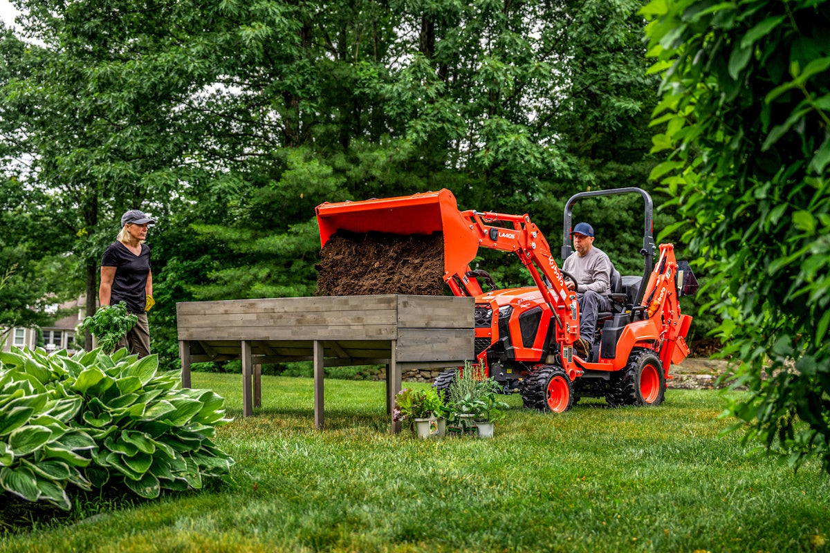 Kubota BX90 series tractor-loader-backhoe filling a raised garden bed with its front loader