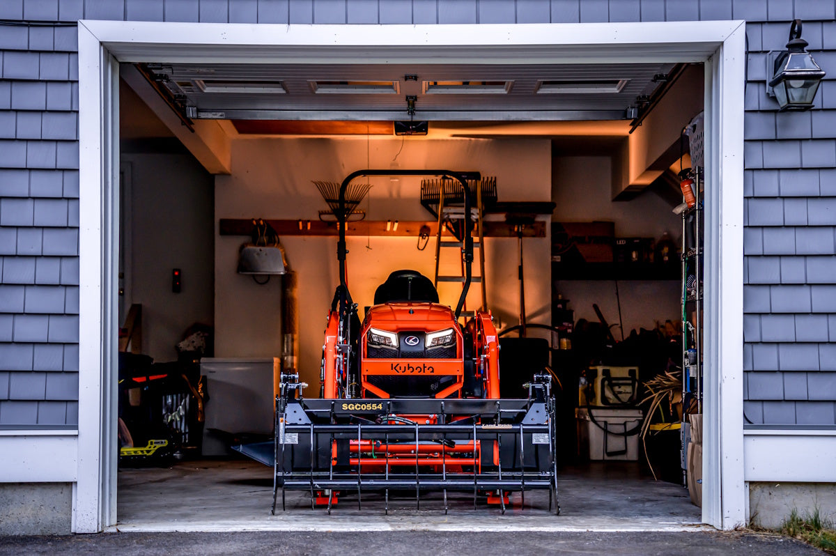 Kubota BX90 series sub-compact tractor with a grapple on its loader, parked in a garage