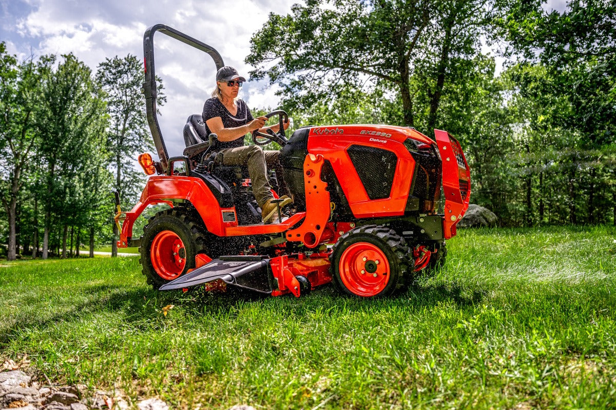 Kubota BX2390 Deluxe sub-compact tractor mowing a lawn with a mid-mount deck