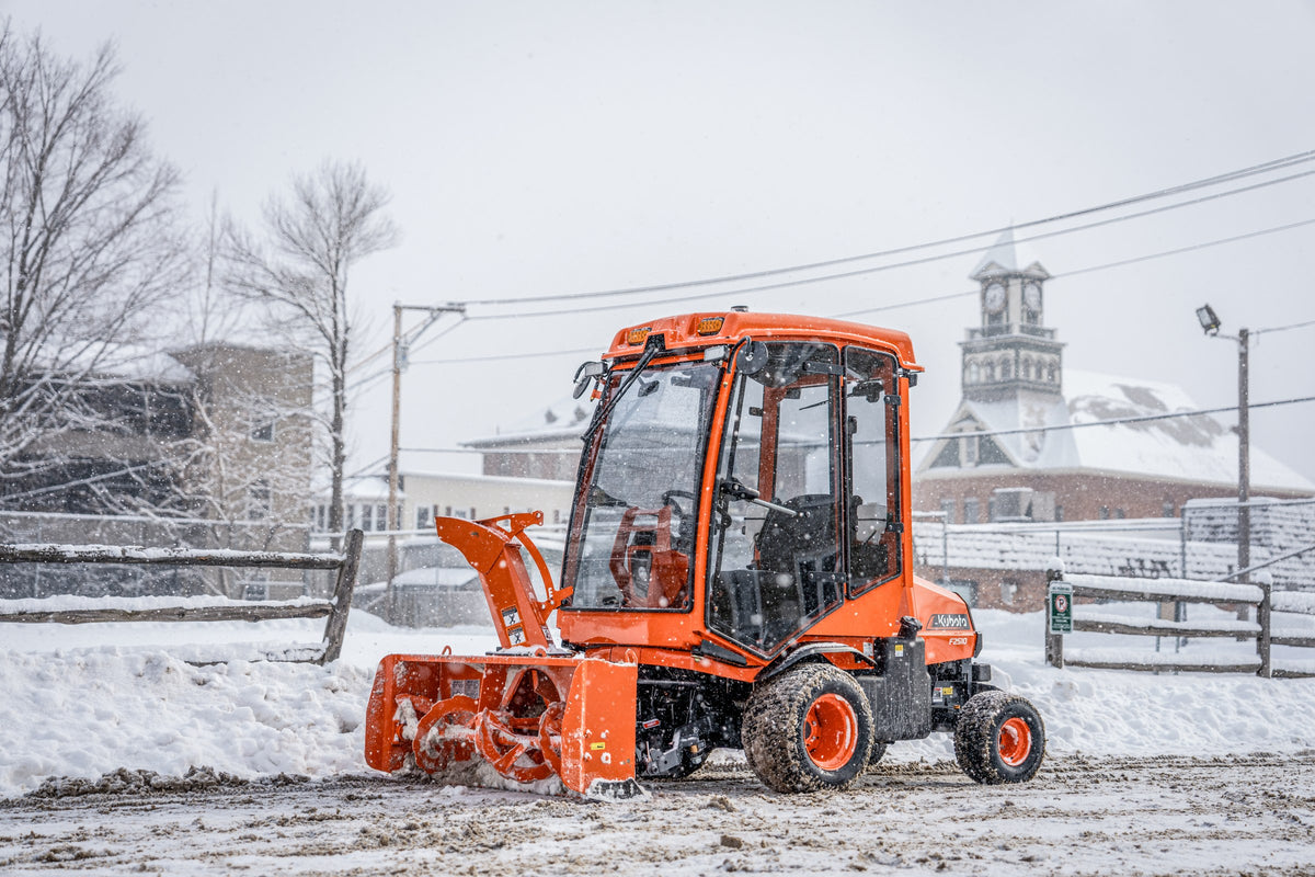 Kubota front-mount tractor with a cab and snow blower clearing a street