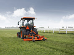 Kubota tractor with a cab mowing a lawn with a Land Pride FDR25 series grooming mower, rear view by a white fence