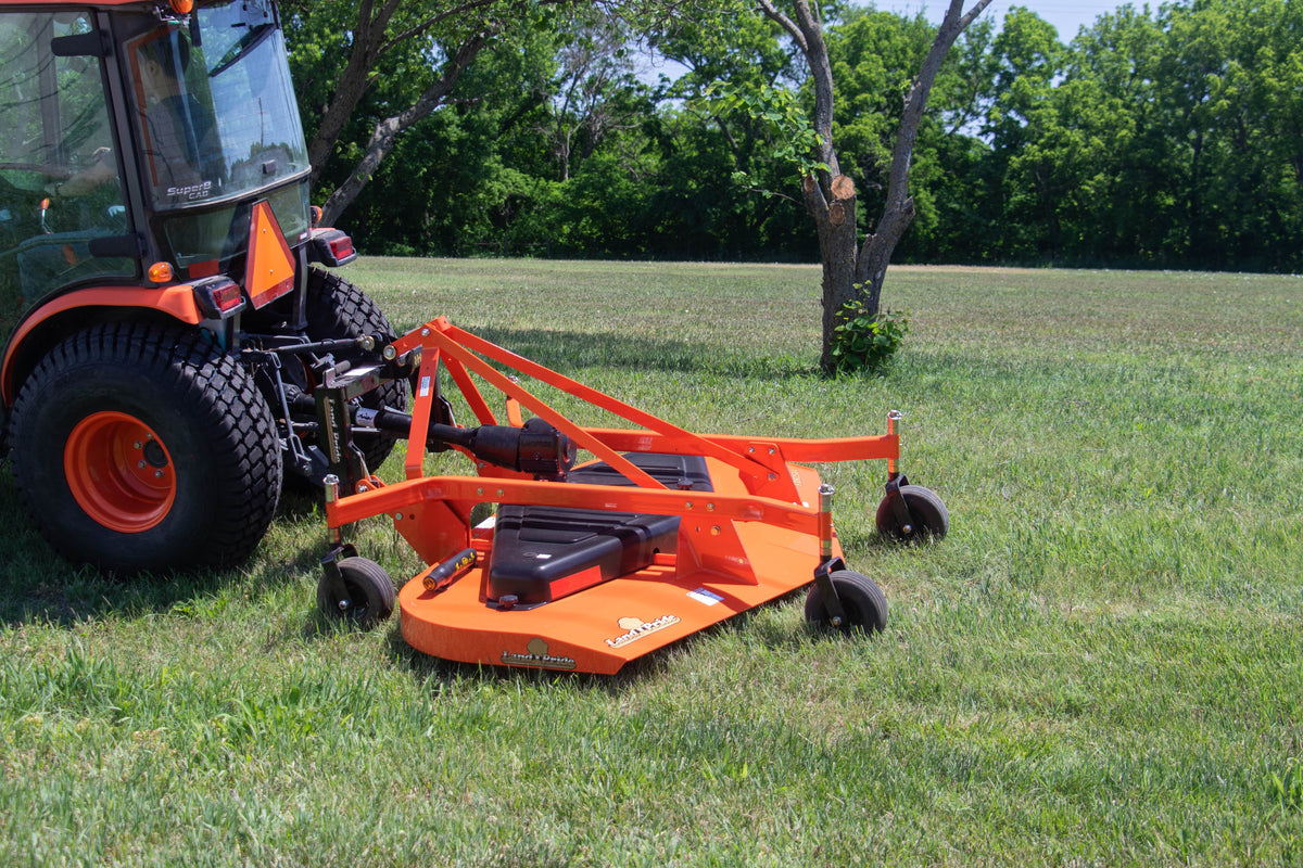 Land Pride FDR25 series grooming mower behind a Kubota tractor with a cab, on a lawn by a stand of trees