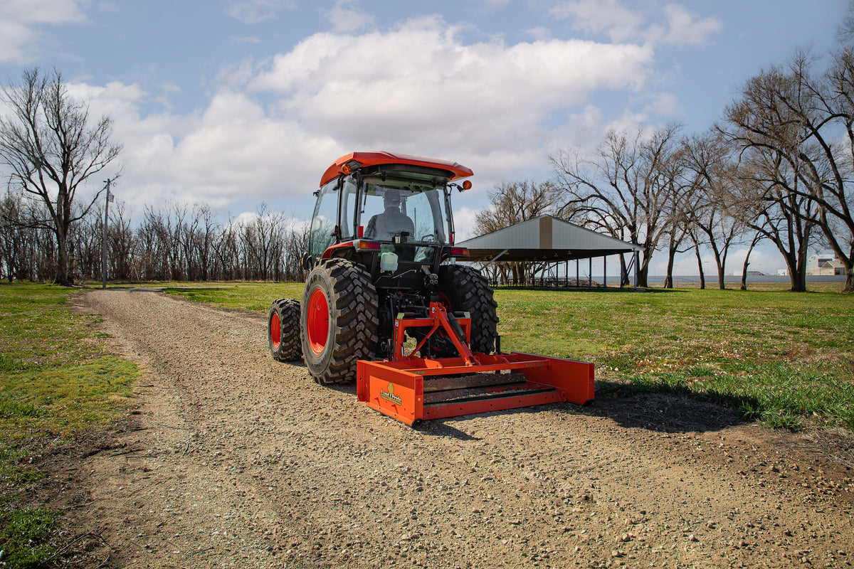 Kubota tractor with a cab grading a gravel drive with a Land Pride GS15 series grading scraper, a picnic shelter behind