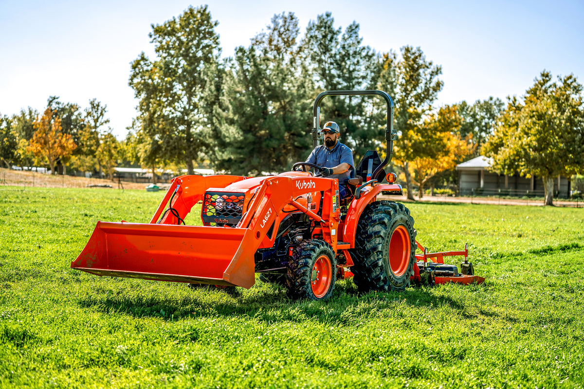Kubota L3902 tractor with a front loader and a rear finish mower, parked on a lawn with its operator in the seat