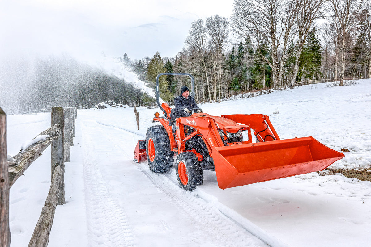 Kubota L series tractor with an LA627 front loader and a rear snowblower, clearing a snowy lane