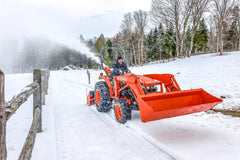 Kubota L series tractor with an LA627 front loader and a rear snowblower, clearing a snowy lane