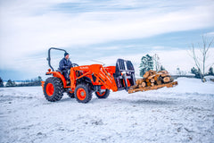 Kubota L series tractor with an LA627 front loader, carrying firewood on pallet forks in the snow