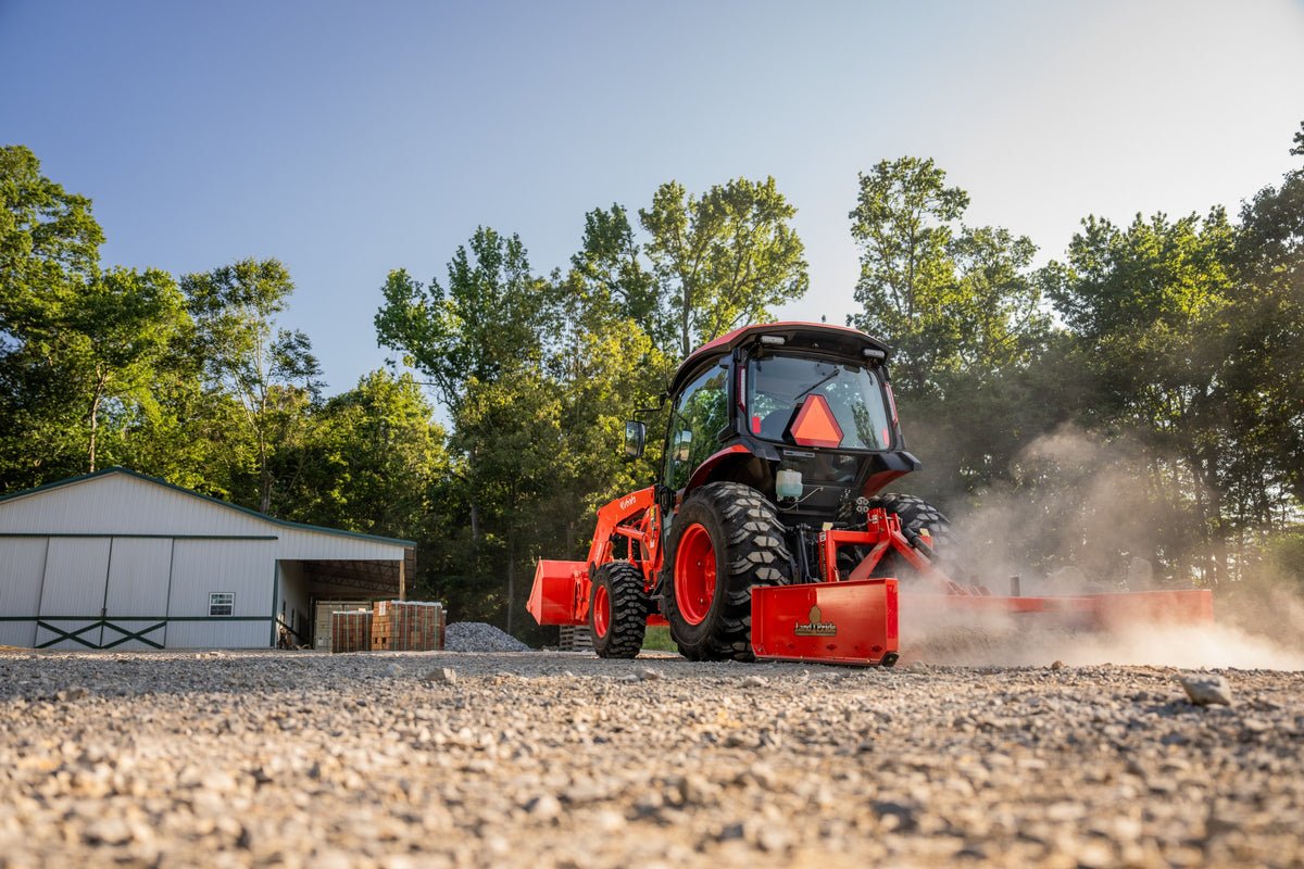 Kubota L6070 ProCab from behind, grading a gravel yard with a box blade