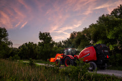 Kubota M7 series cab tractor with a front loader and a Kubota BV5200 round baler at dusk