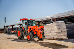Kubota MX4900 Cab moving a pallet of bagged bedding with pallet forks at a horse barn