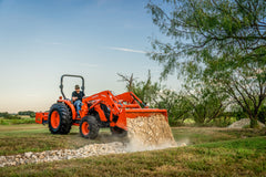 Kubota MX4900 dumping rock from its loader bucket in a grassy yard