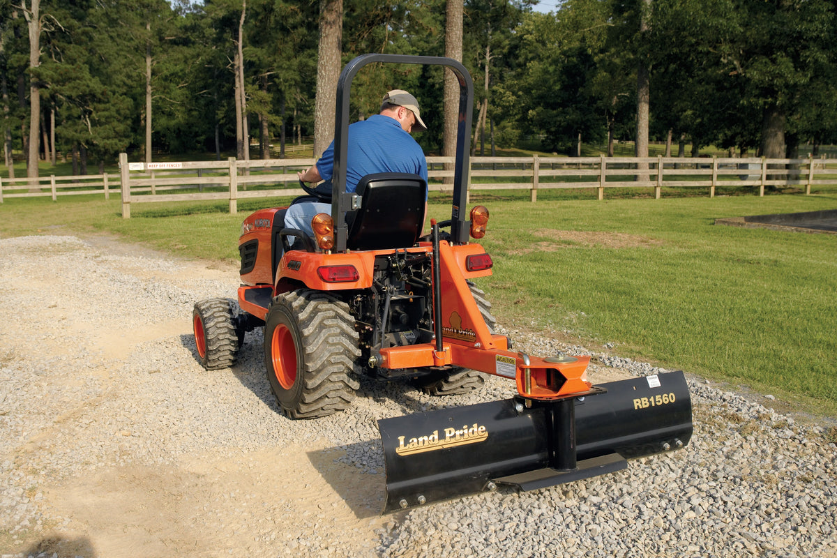 A man grading a gravel drive with a Land Pride RB1560 rear blade on a Kubota sub-compact tractor