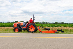 A man mowing a roadside with a Land Pride RCR1884 rotary cutter behind a Kubota L5060 tractor, a cornfield behind