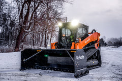 Kubota compact track loader with its lights on and a Kubota snow pusher, in snow at dusk