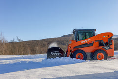 Kubota SSV75 skid steer clearing snow with a Kubota SSP2596 snow pusher, hills behind