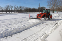Kubota tractor with a cab and front loader clearing a snowy lot with a Land Pride STB15 series snow trip blade