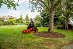 Kubota Z232 zero-turn mower mowing around a mulched tree, a large house behind