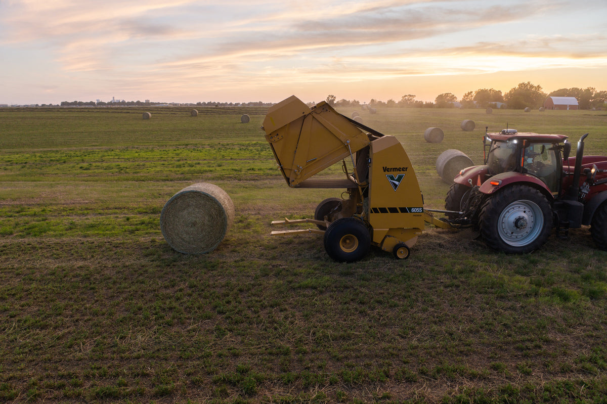 Aerial view of Vermeer 605S Premium round baler ejecting a bale at sunset