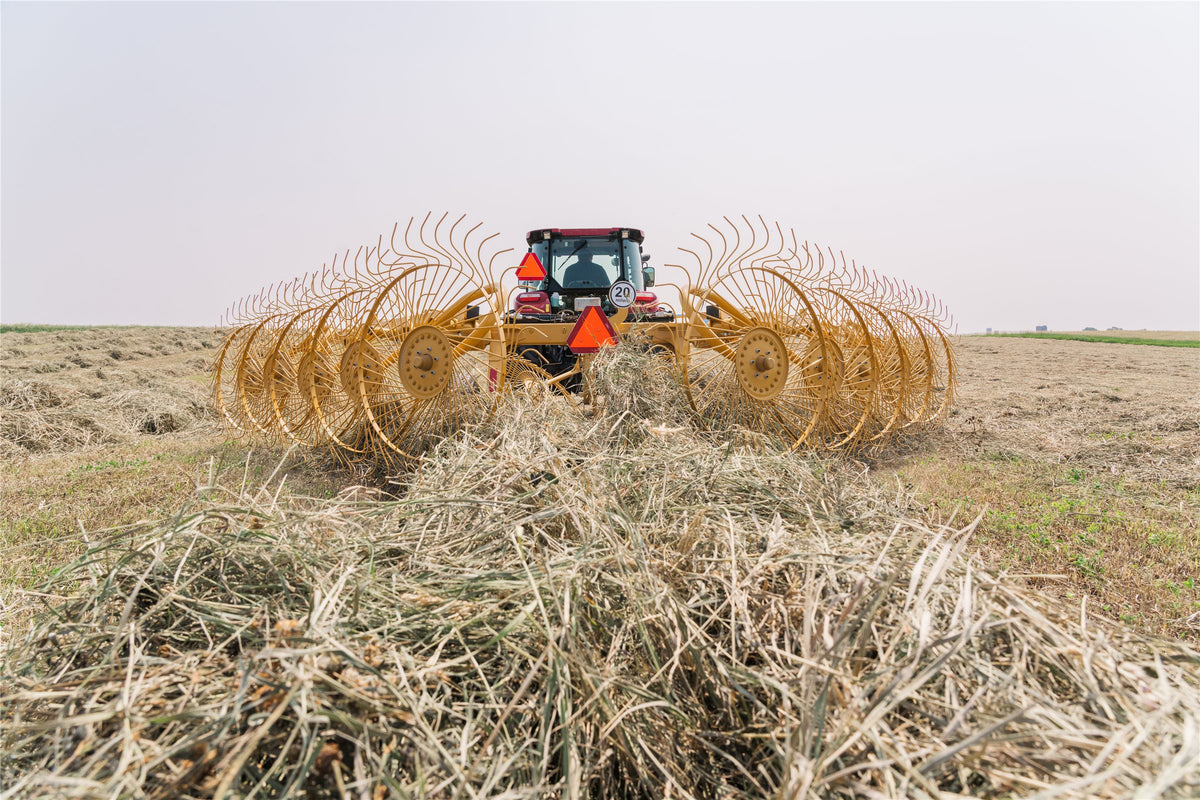 Vermeer VRC1022 carted wheel rake behind a red tractor, raking hay into a windrow, seen from behind