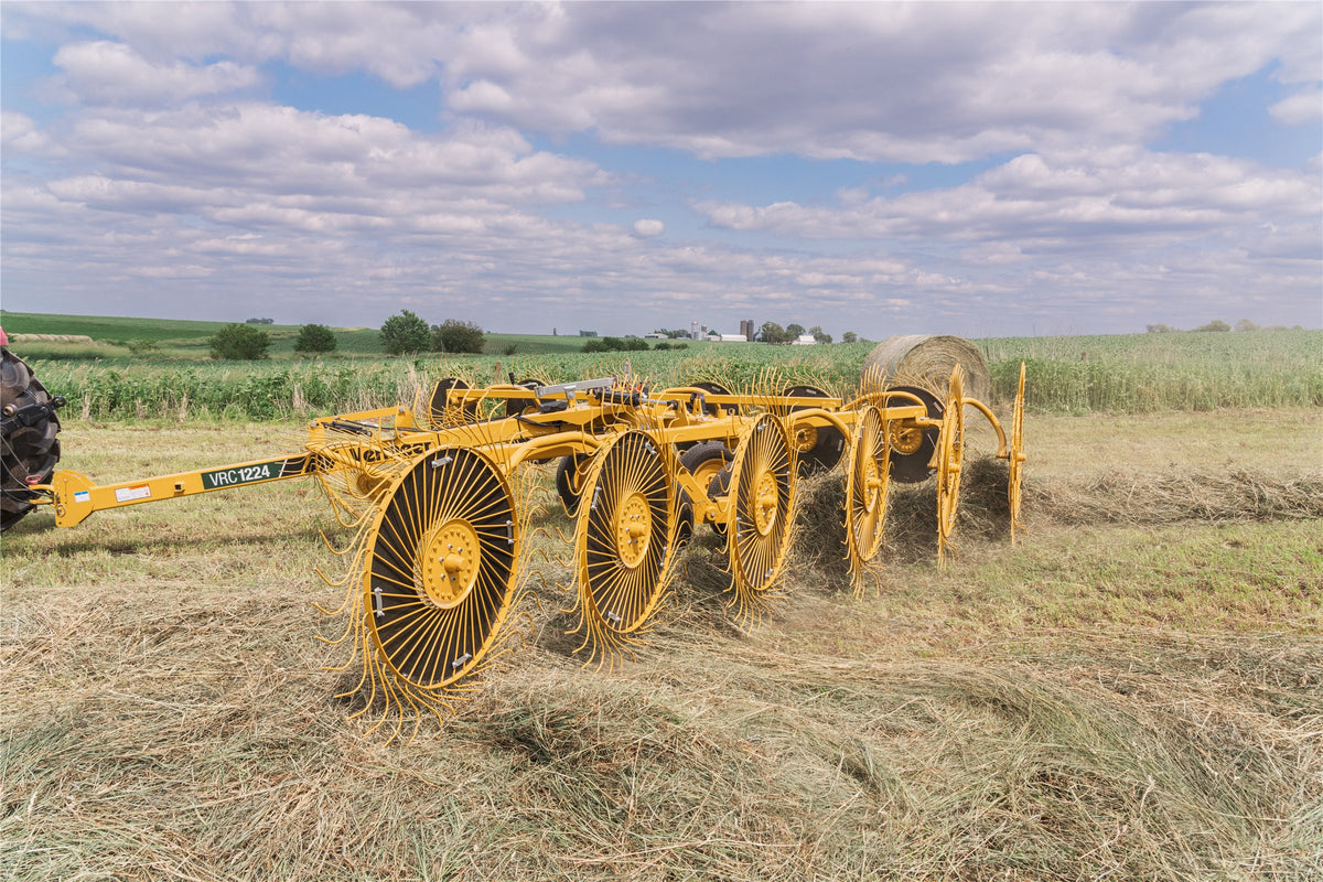 Vermeer VRC1224 carted wheel rake raking hay in a field, a round bale behind it