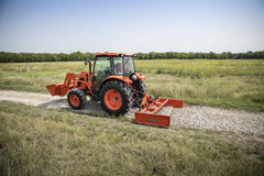 A Kubota tractor with a front loader smoothing a gravel track with a Land Pride GS25 series grading scraper, tall grass alongside
