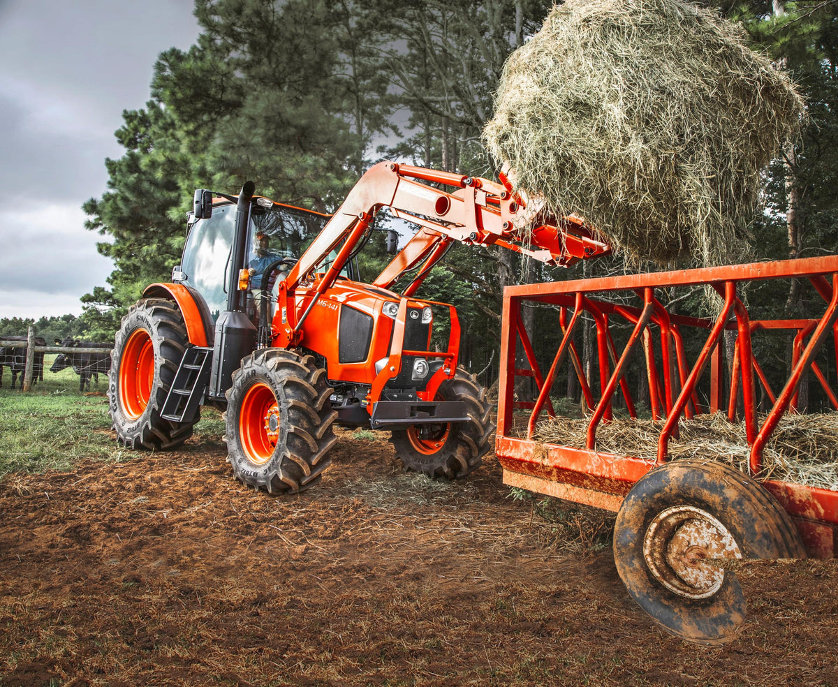 Kubota M6 series cab tractor with a front loader, setting a round bale in a hay feeder