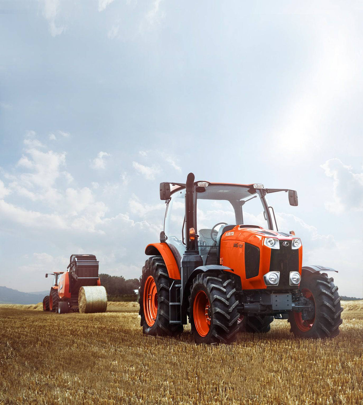 Kubota M6 series cab tractor in a stubble field, a Kubota round baler behind it