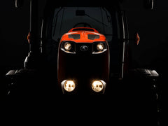 The front of a Kubota M6 series tractor with its lights on, in the dark