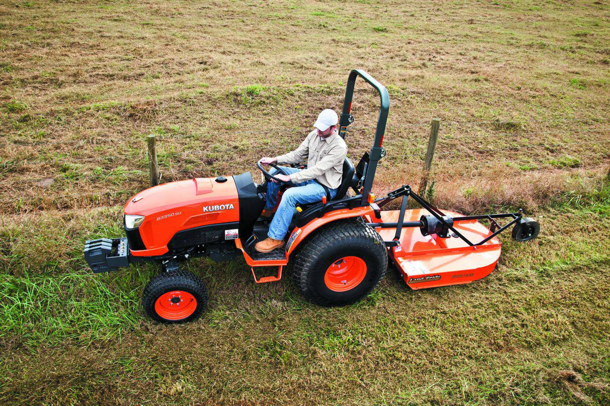 A man mowing tall grass on a slope with a Land Pride RCR1248 rotary cutter behind a Kubota compact tractor