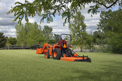 A man mowing a park lawn with a Land Pride RCR18 series rotary cutter behind a Kubota compact tractor with a front loader
