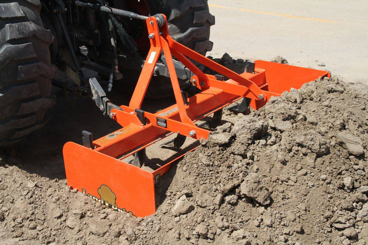 A Land Pride BB12 series box scraper pushing a pile of dirt, close up behind a tractor's rear tire