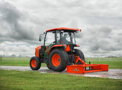 Kubota tractor with a cab pulling a Land Pride GS15 series grading scraper along a gravel lane