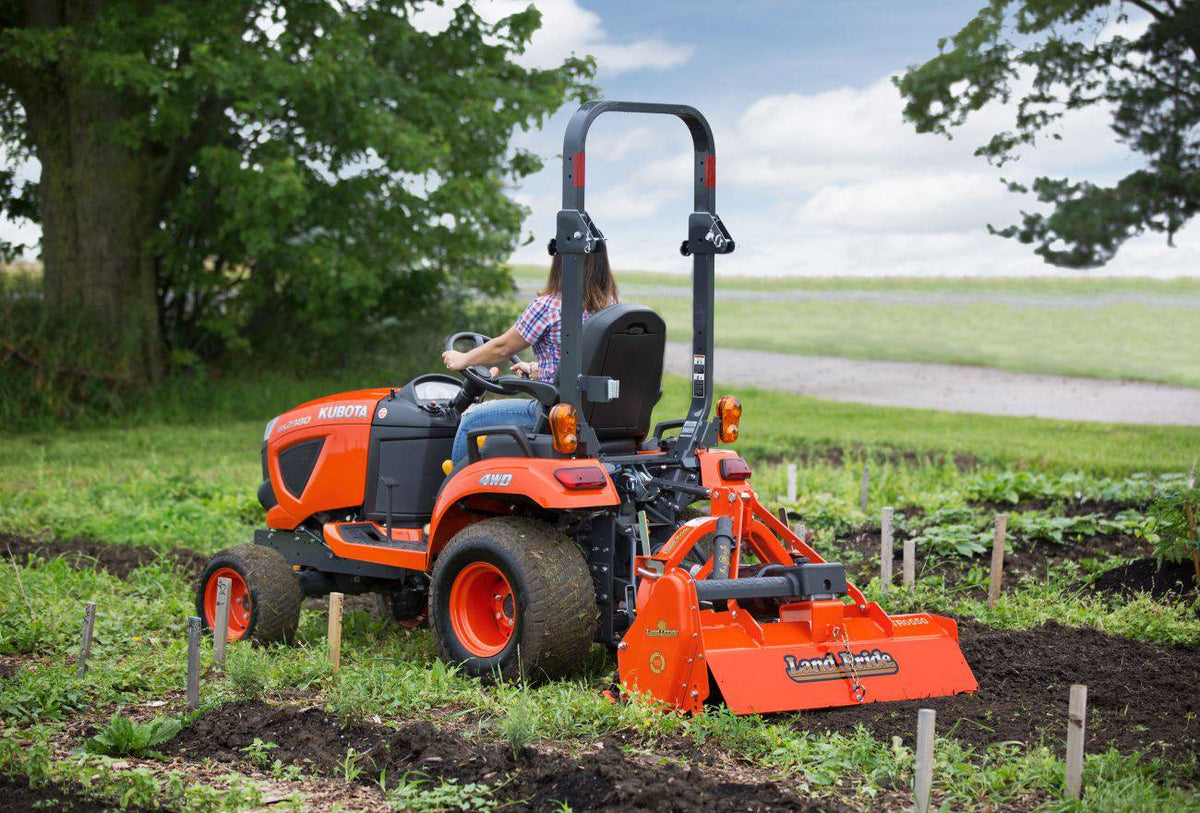 Land Pride RTR05 series rotary tiller on a Kubota sub-compact tractor in a vegetable garden, rear three-quarter view