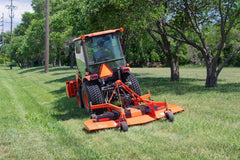 Kubota compact tractor with a cab mowing a park lawn under trees with a Land Pride FDR25 series grooming mower
