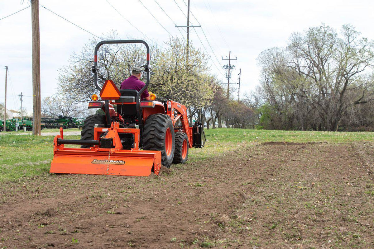 Kubota compact tractor with a front loader tilling a strip of field with a Land Pride RTR12 series rotary tiller