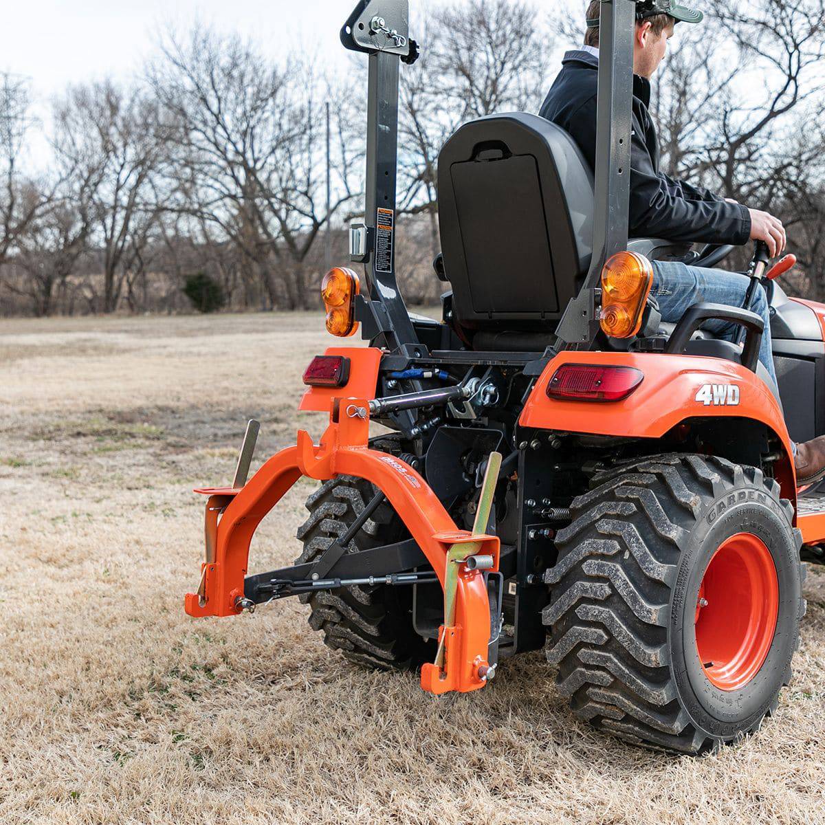 A man on a Kubota sub-compact tractor with a Land Pride QH05 quick hitch on its 3-point hitch, seen from behind