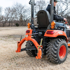 A man on a Kubota sub-compact tractor with a Land Pride QH05 quick hitch on its 3-point hitch, seen from behind