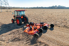 A Kubota tractor with a cab pulling a Land Pride RC25 series folding rotary cutter across a dry field