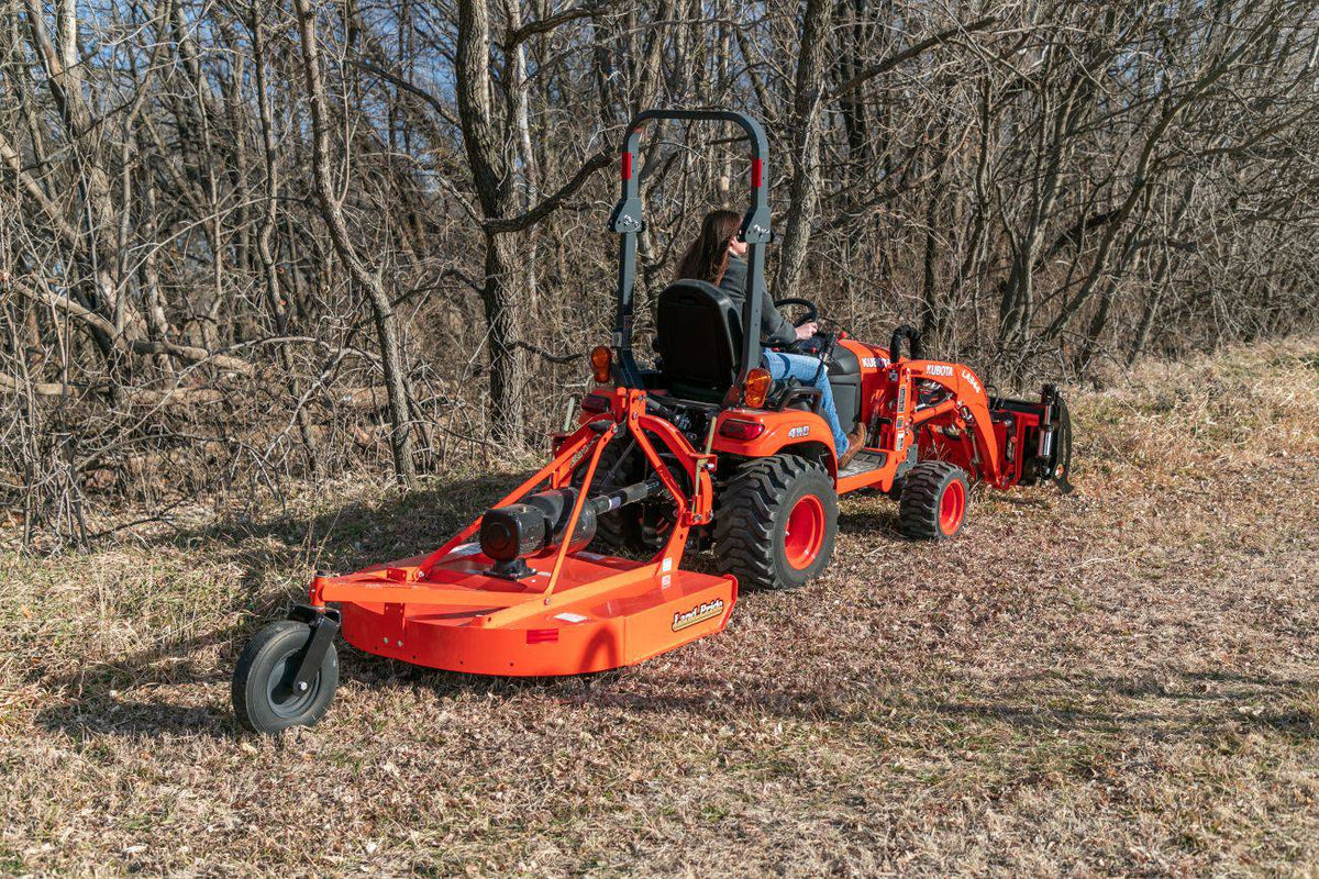 A woman on a Kubota sub-compact tractor with a front loader, cutting brush with a Land Pride RCR12 series rotary cutter, rear view
