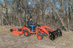 A man cutting brush with a Land Pride RCR12 series rotary cutter on a Kubota sub-compact tractor with a grapple