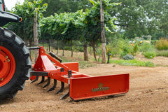 A Land Pride GS25 series grading scraper with its scarifier shanks down, behind a Kubota tractor in a vineyard