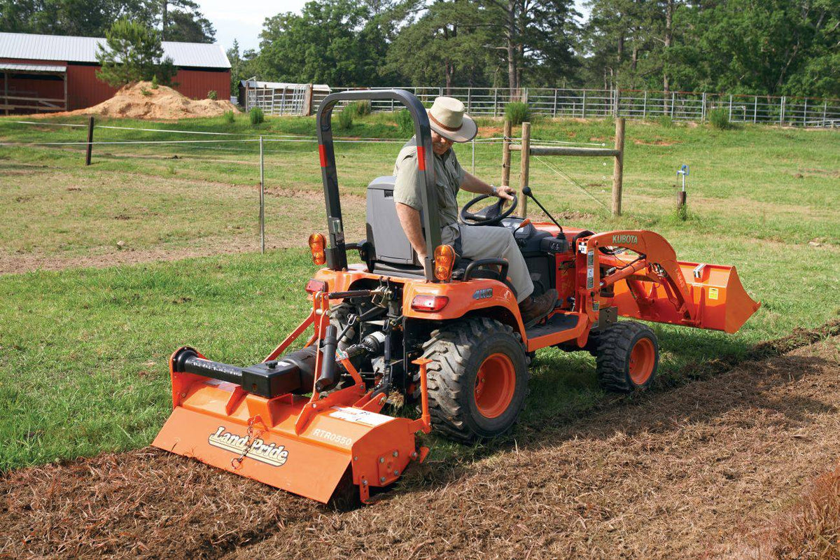 A man tilling a garden plot with a Land Pride RTR05 series rotary tiller on a Kubota sub-compact tractor with a front loader